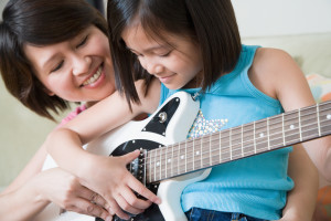 Mother teaching daughter how to play guitar